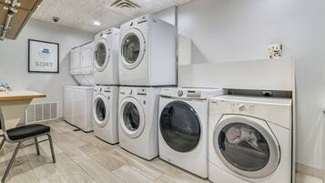 A laundry room with multiple washing machines, a chair, and a wall-mounted shelf.