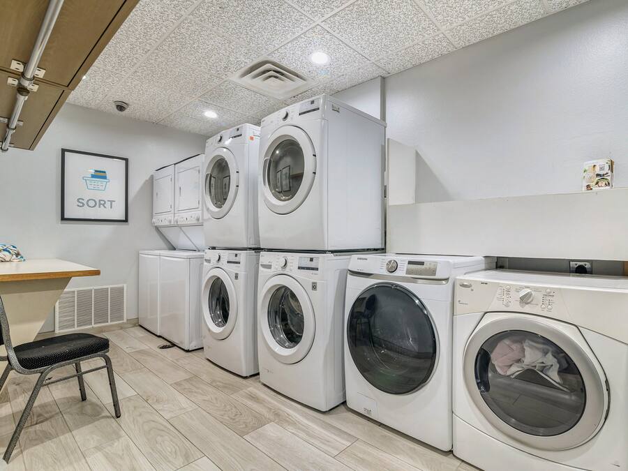 A laundry room with multiple washing machines, a chair, and a wall-mounted shelf.