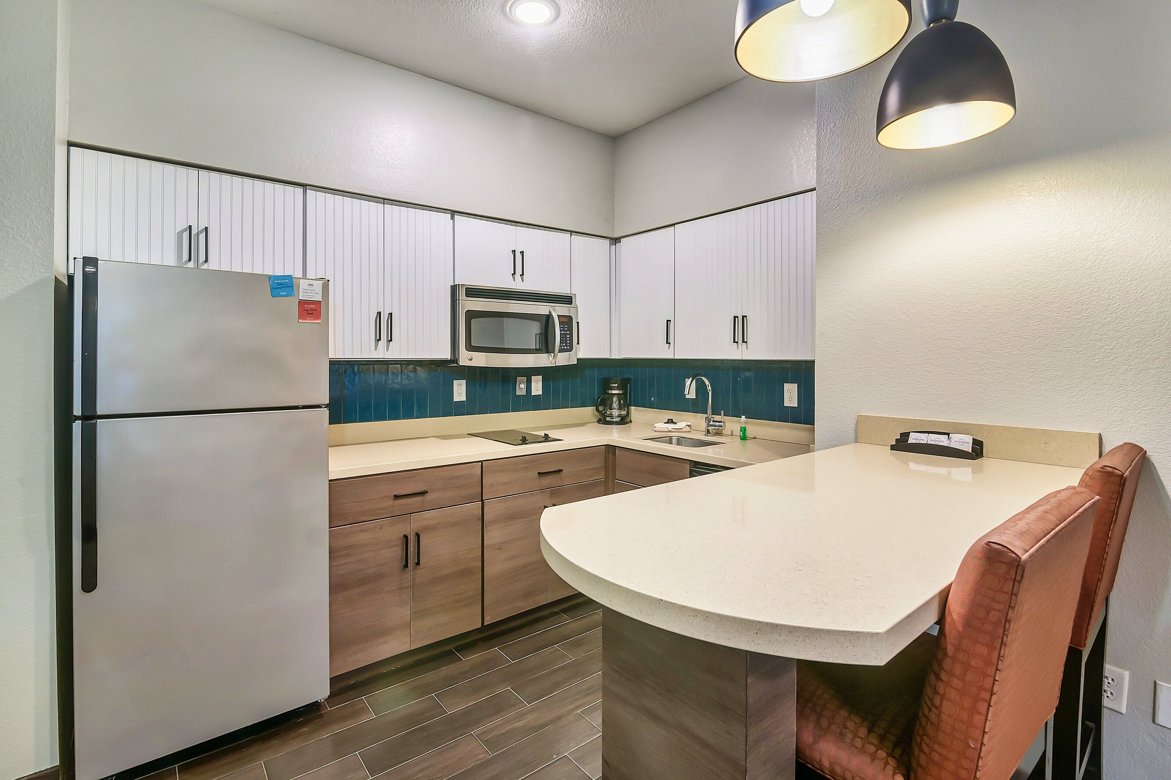 Cocina compacta con refrigerador, microondas, pileta y una isla curva con una silla.
