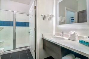 A bathroom with a glass shower enclosure, a white sink, and a mirror above it. - Staybridge Suites University Area by IHG (Tyler)