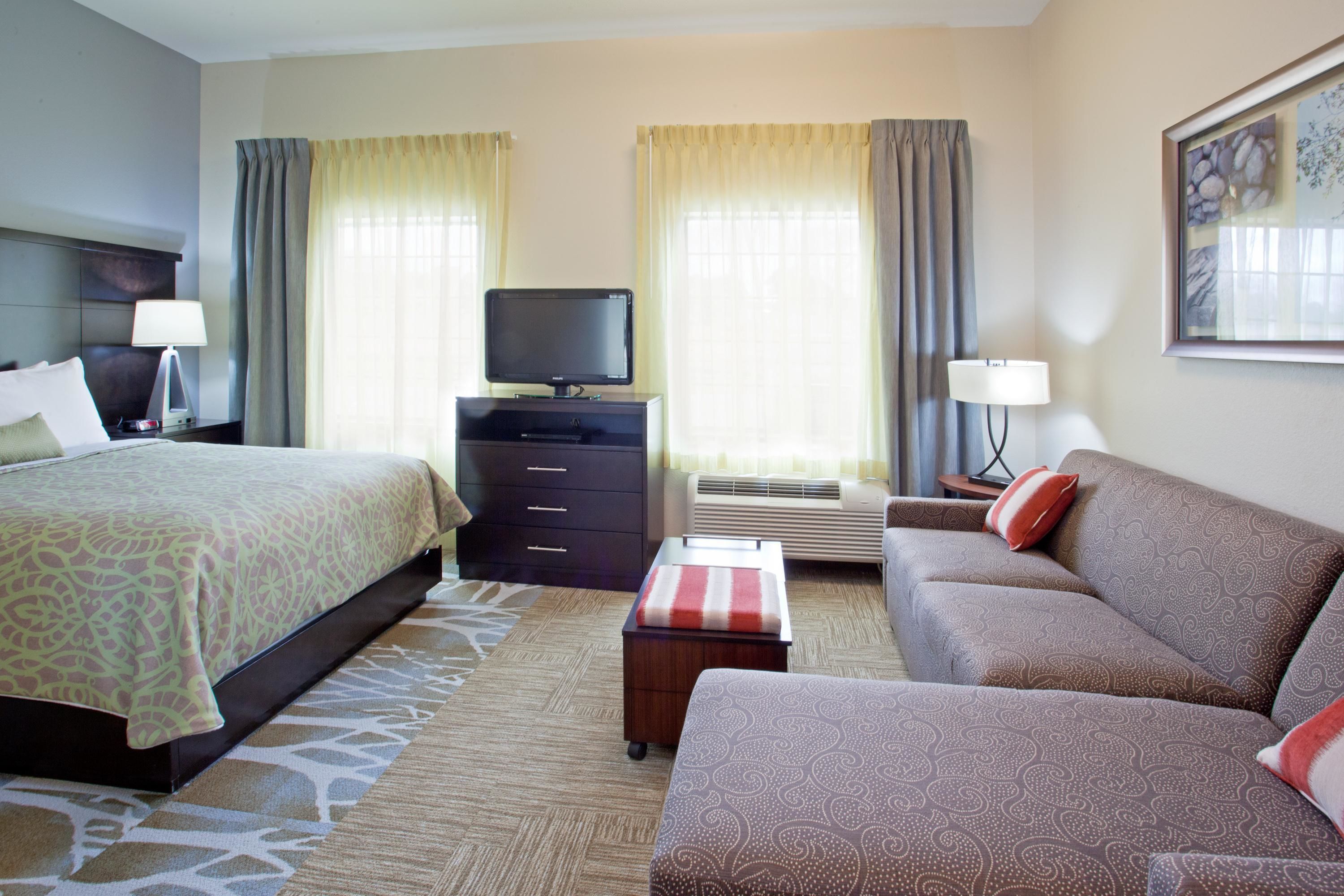 Une chambre d’hôtel avec un lit, un canapé, une télévision et un bureau avec une lampe.