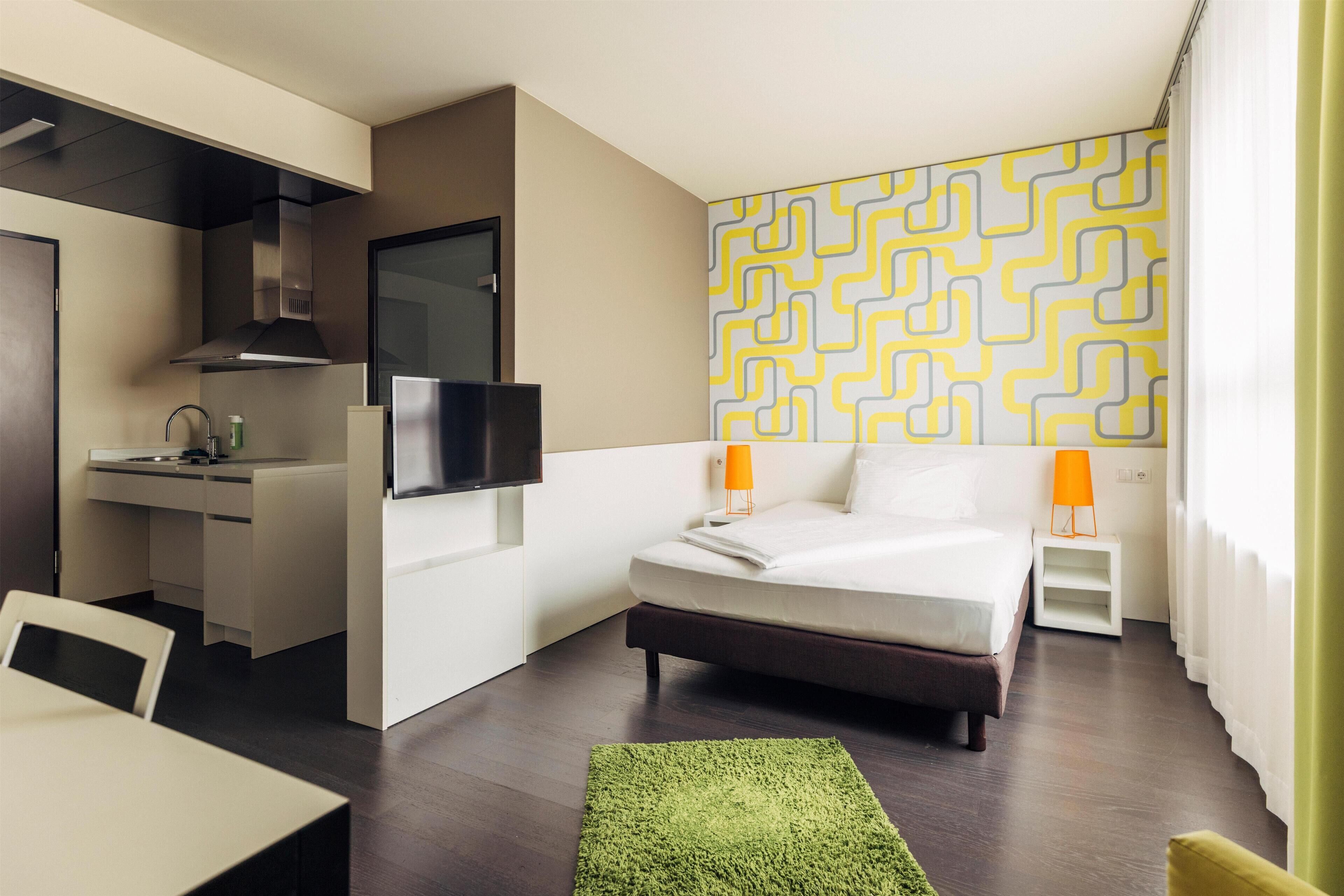 A modern hotel room with a bed, a desk, a TV, and a patterned wall.