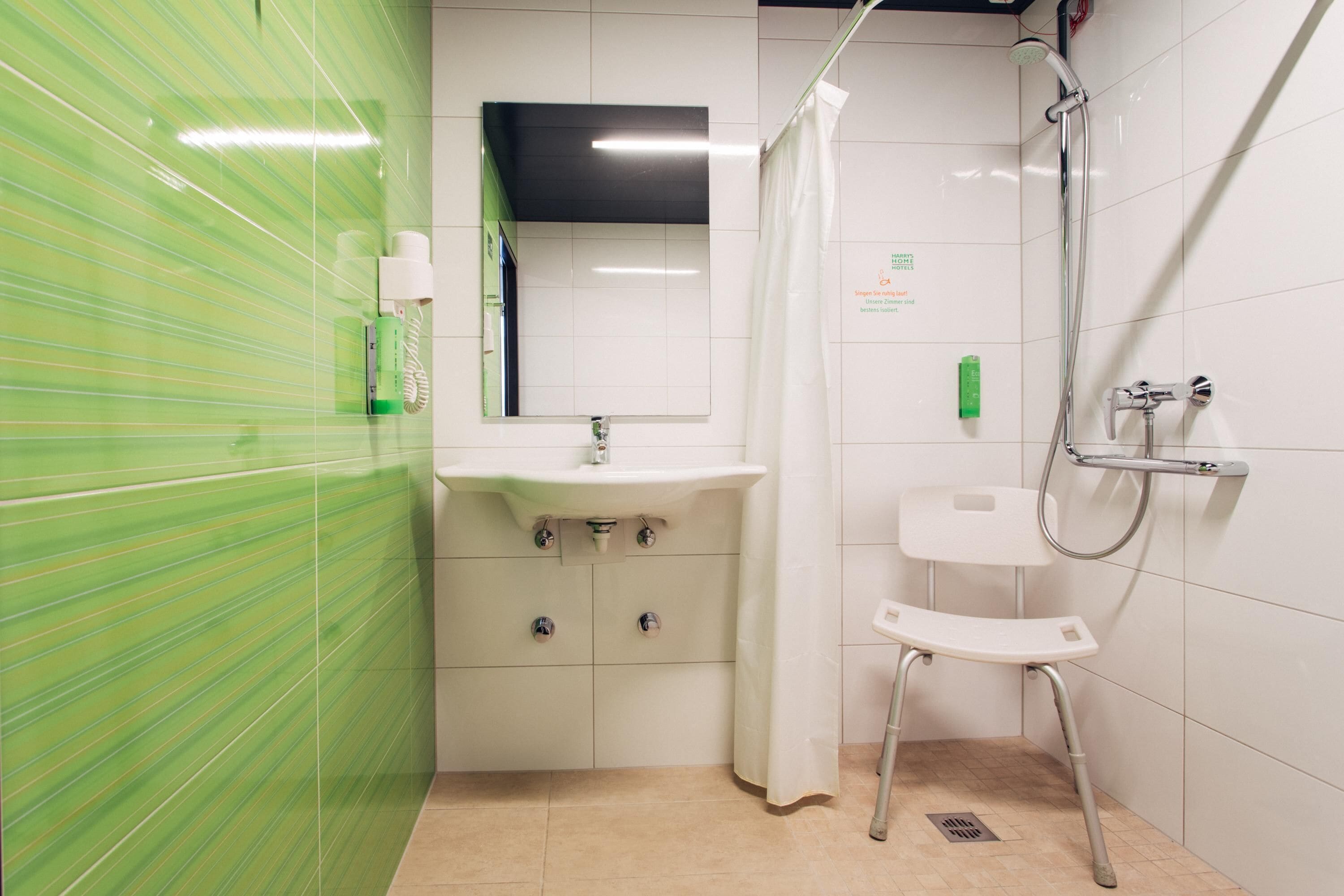 A bathroom with a green-striped wall, a white sink with a mirror, a shower with a handheld showerhead, and a white toilet.