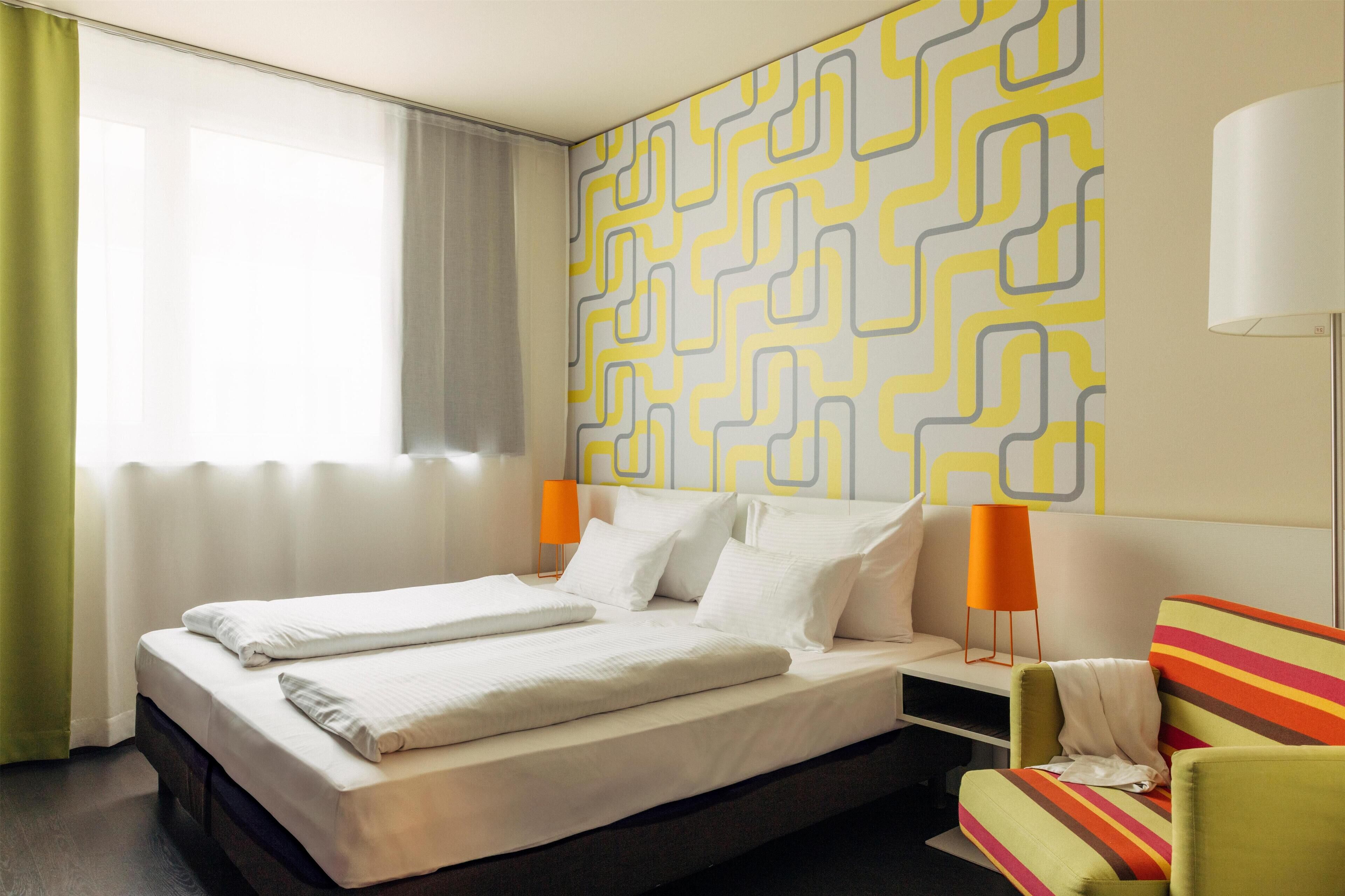 Quarto de hotel com cama, mesa de cabeceira, abajur e uma cadeira.