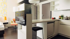 Een moderne keuken met witte kasten, een zwart aanrecht en een ingebouwde oven. Er is een klein barretje met een kruk en een tv aan de muur.