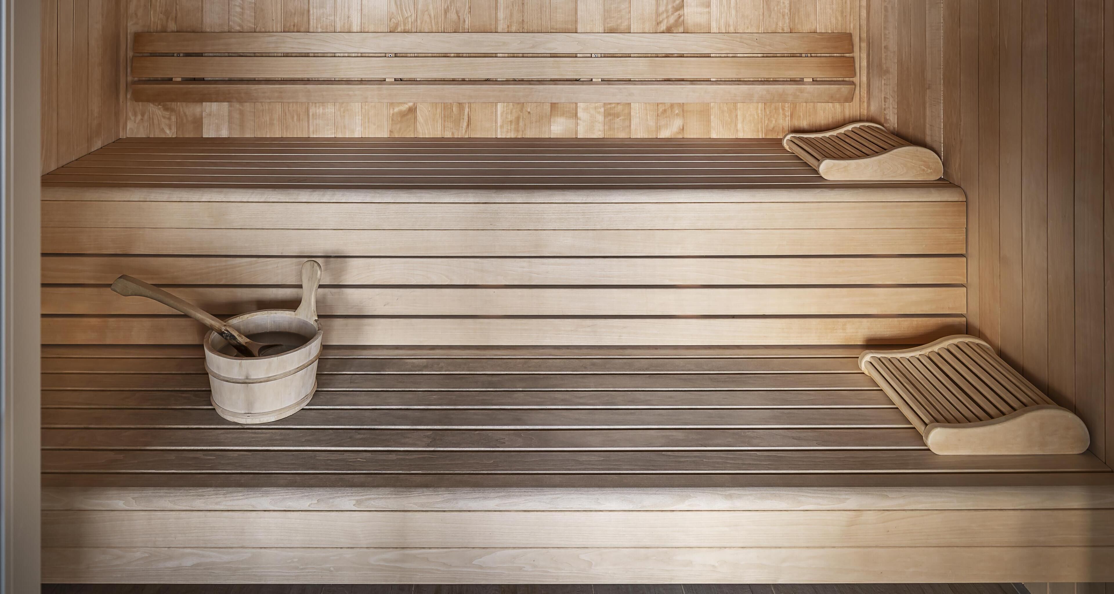 Una sauna con panche in legno e un catino di legno con una schiumarola.