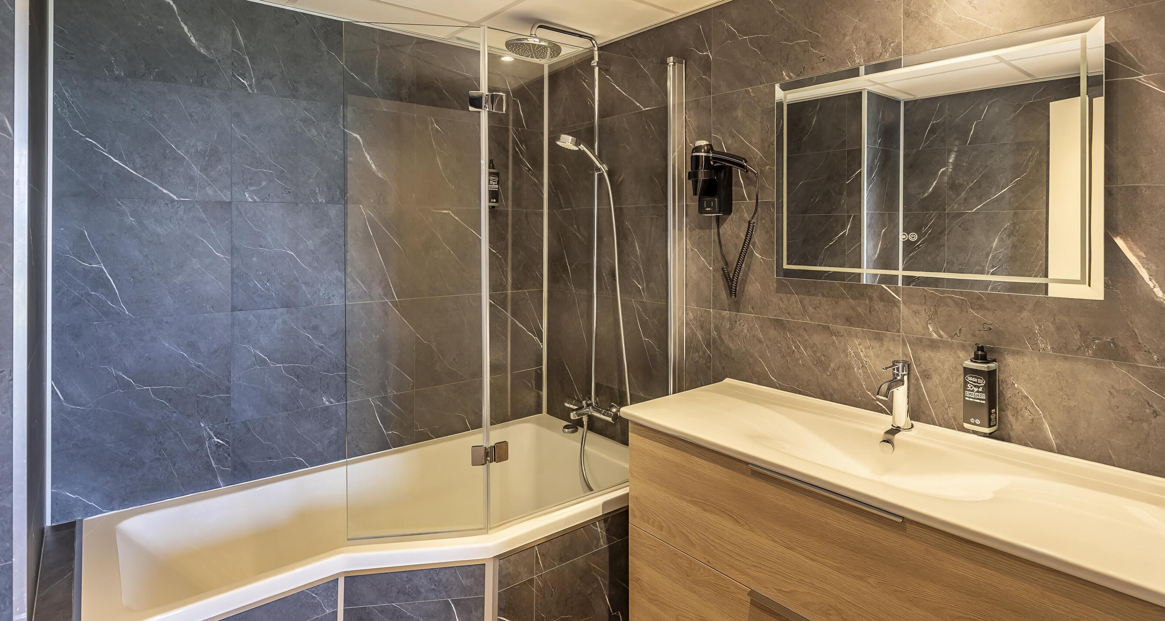 Un baño moderno con ducha envuelta en vidrio, tocador con espejo y paredes de mármol.