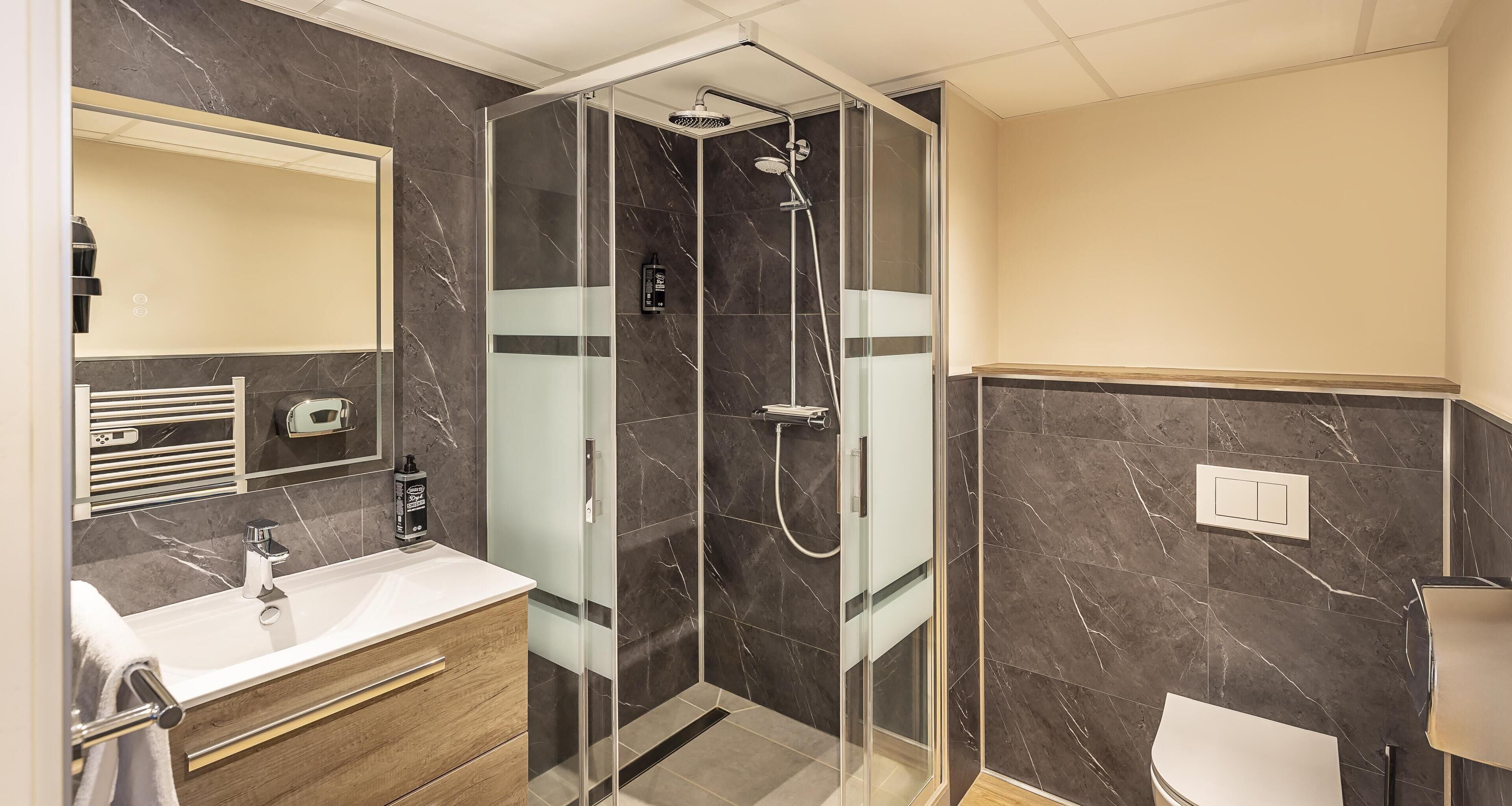 A modern bathroom with a glass-enclosed shower, a white sink, and a wooden vanity.