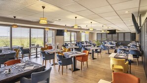 Un ristorante moderno con diversi tavoli e sedie, ampie finestre e ventilatori a soffitto.