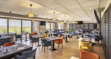 Un restaurante moderno con varias mesas y sillas, ventanas amplias y ventiladores de techo.