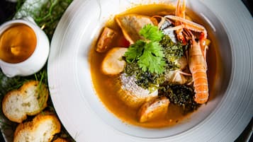 Una sopa de mariscos con pan y una copa de vino blanco sobre una mesa.
