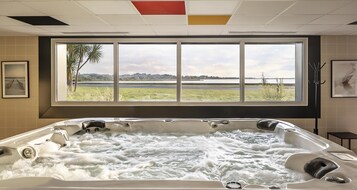 Un jacuzzi con vista a un lago y palmeras a través de un ventanal grande.