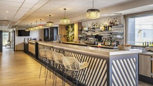 Un'area bar moderna con un lungo bancone, sgabelli in vimini e una selezione di bottiglie e bicchieri sugli scaffali.