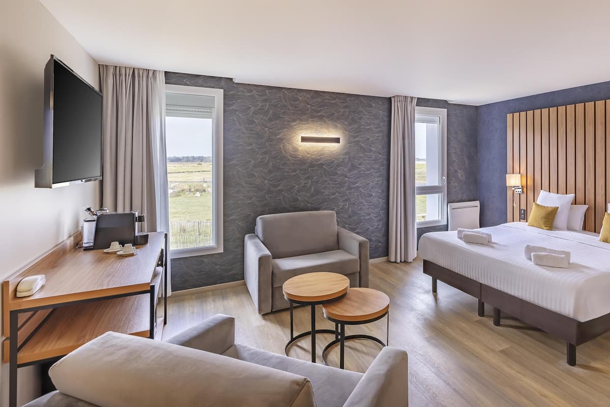 Une chambre d’hôtel avec un lit, un bureau, une chaise, une petite table et un téléviseur.