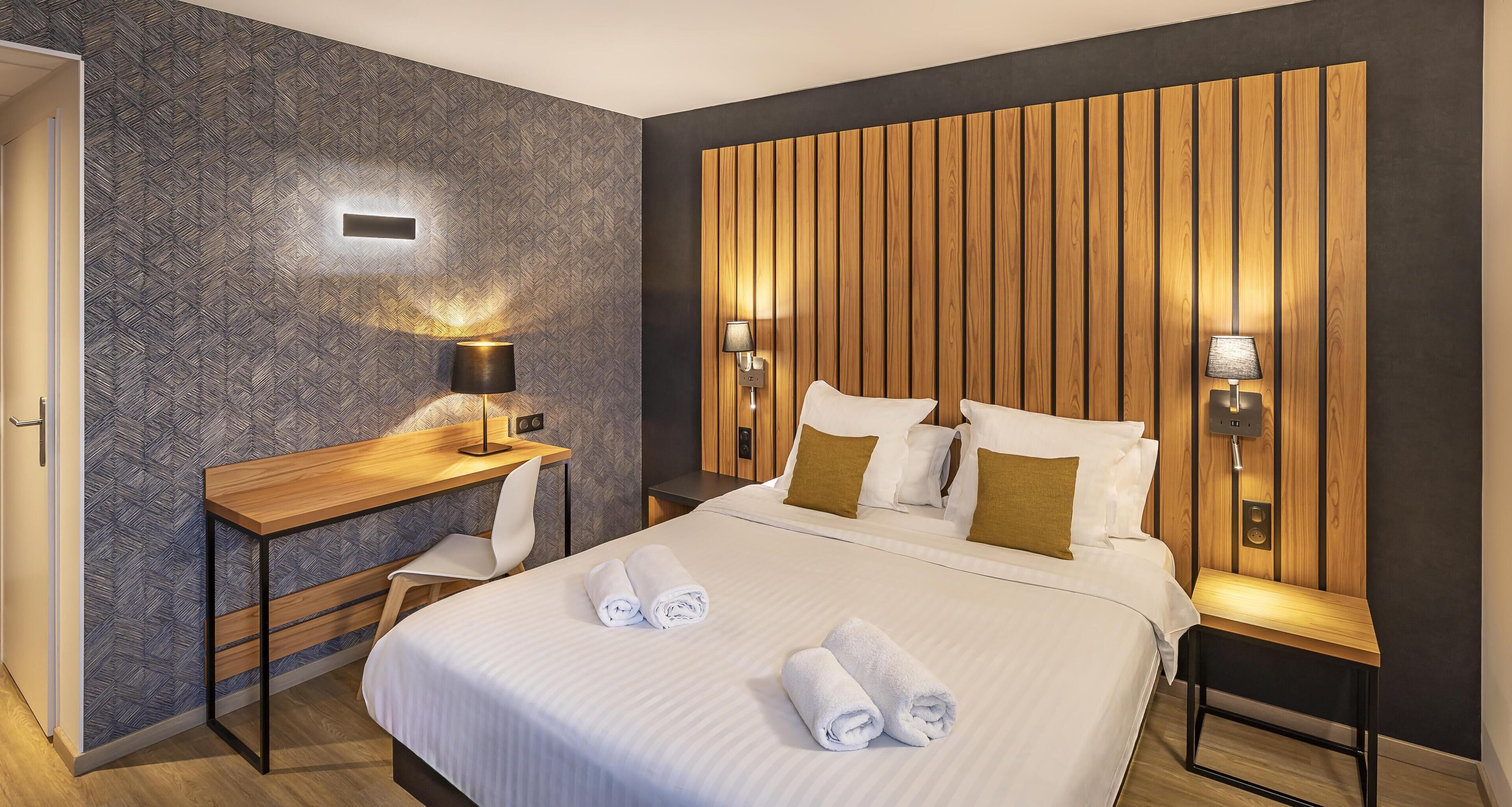 A modern hotel room with a large bed, a wooden desk, and two bedside lamps.