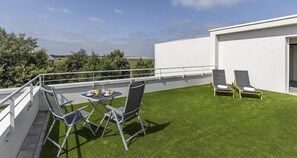 Una terraza en la azotea con mesa y sillas, un sillón de sol y vistas al paisaje.