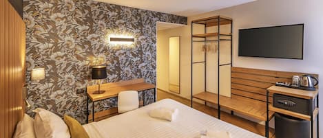A hotel room with a bed, a desk, a chair, a wardrobe, and a TV.