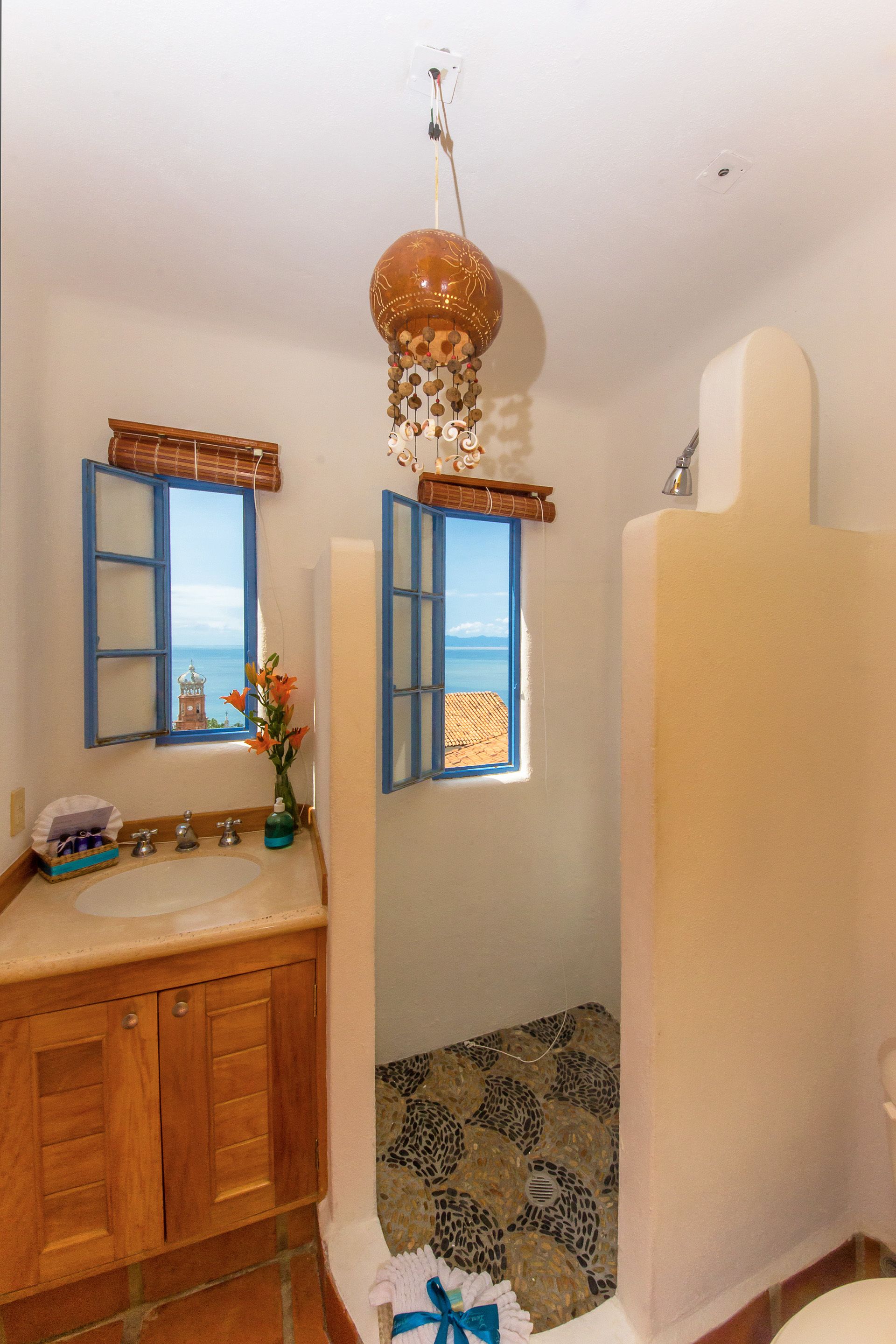 Une salle de bain avec un meuble-lavabo en bois, un grand miroir, un luminaire suspendu et une vue sur la mer par une fenêtre.