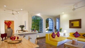 A bright living room with a yellow sofa, a wooden dining table with apples and a knife, and a kitchen area with a sink and potted plants. - Luna Líquida Hotel Boutique (Puerto Vallarta)