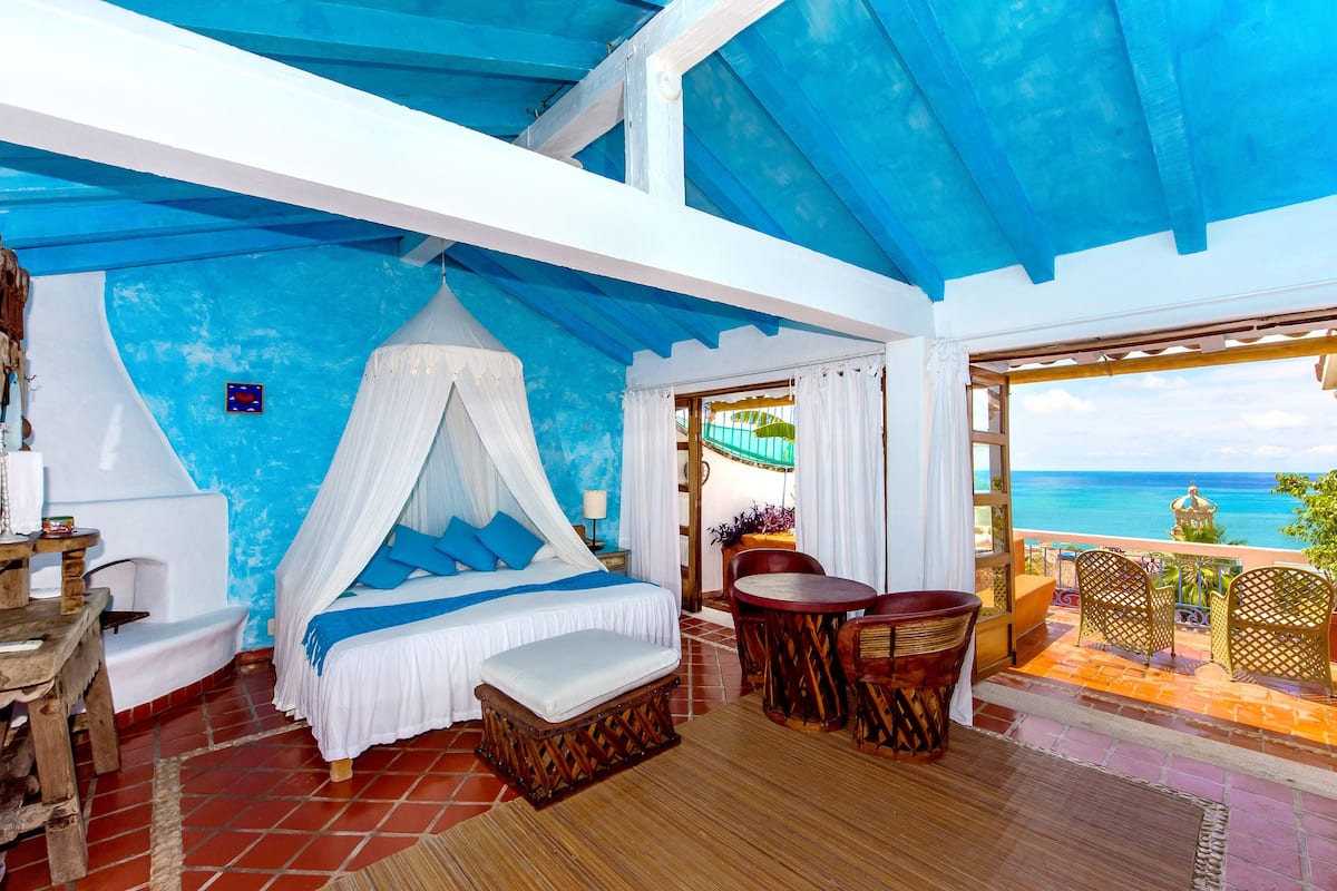 Ein Schlafzimmer mit Bett, Tisch, Stühlen und einem Balkon mit Meerblick.