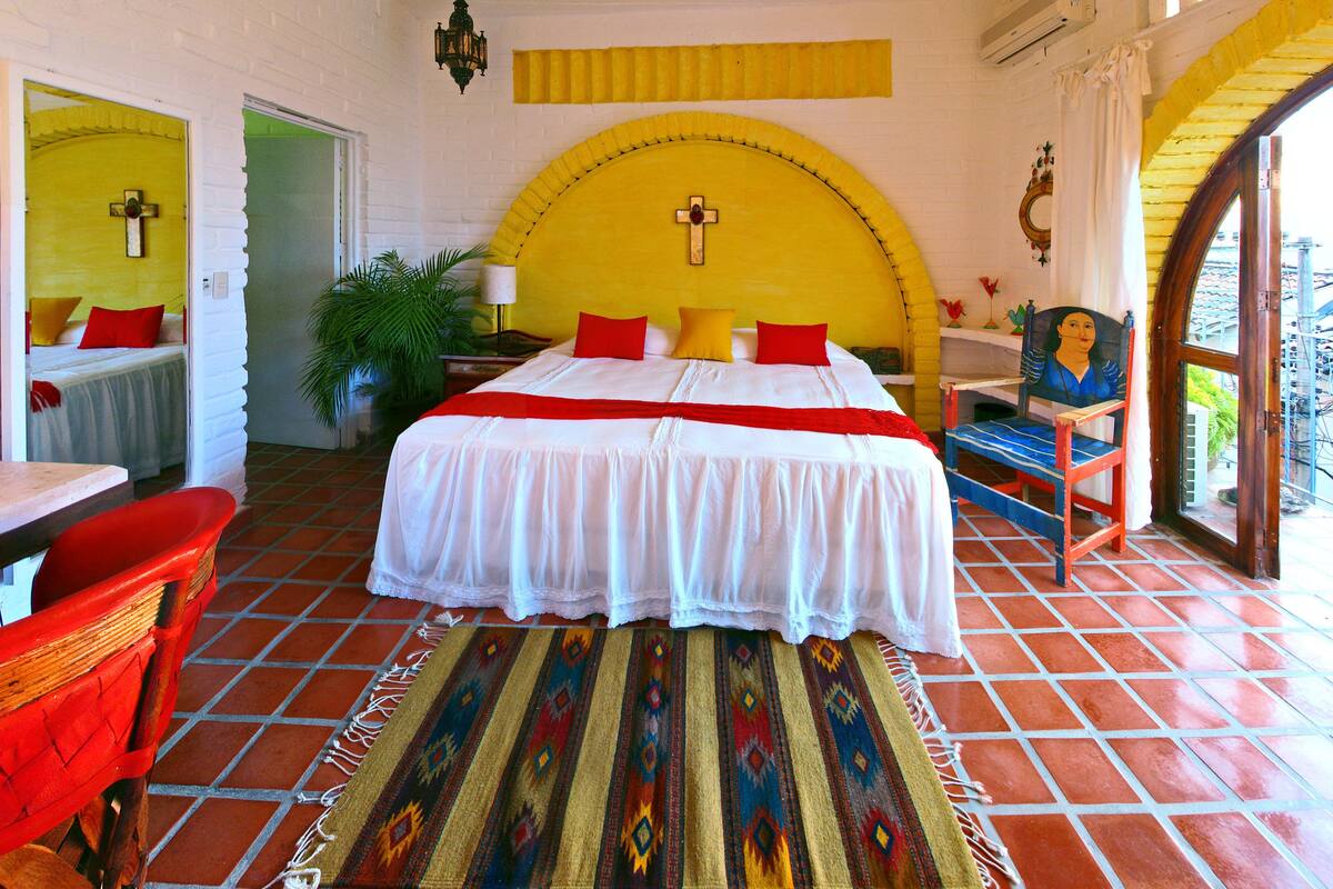 Ein Zimmer mit Bett, Stuhl, Tisch, Lampe und einer Topfpflanze.