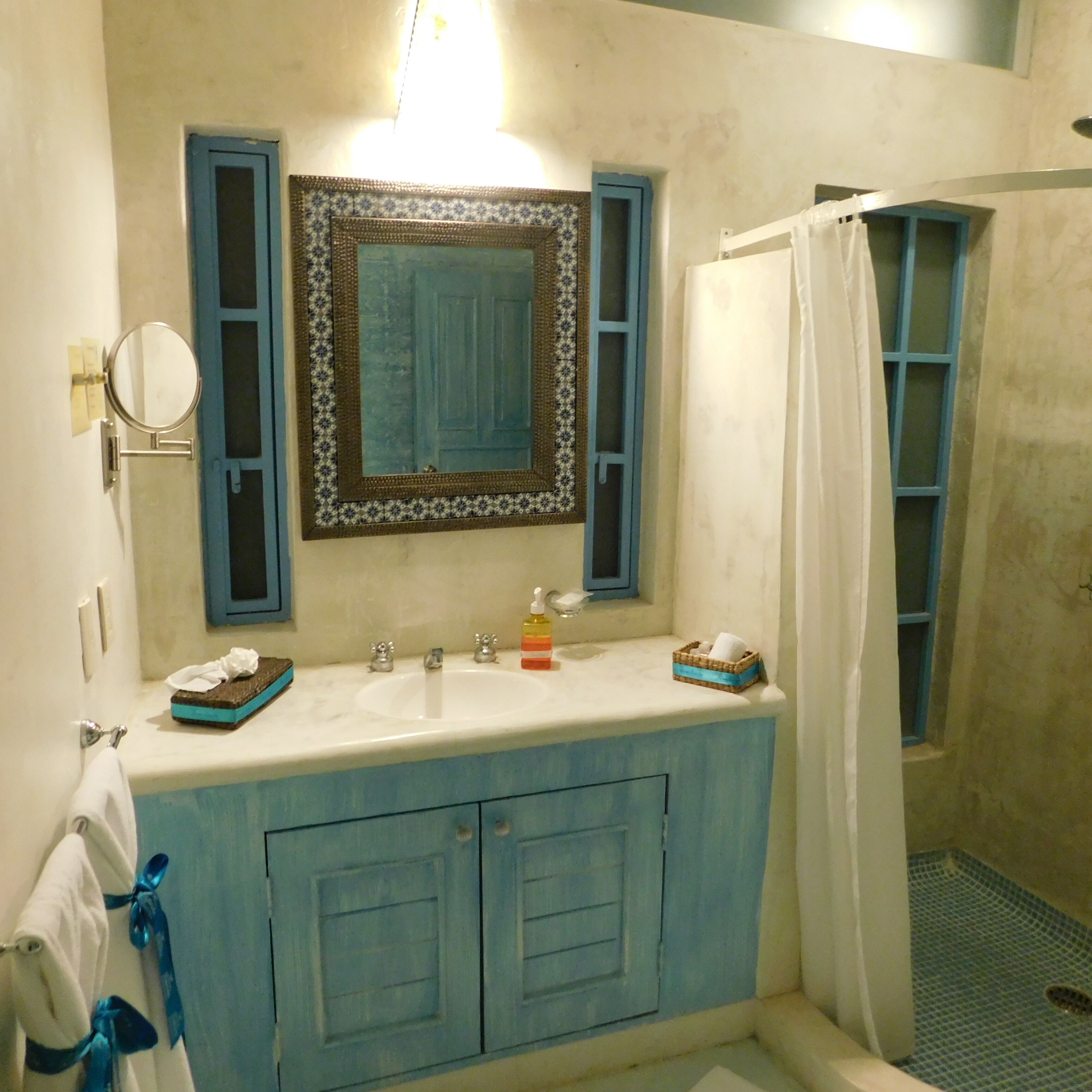 Un baño con tocador azul, espejo, lavabo y zona de ducha.