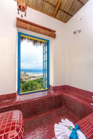 A red-tiled bathroom with a view of a cityscape through a blue-framed window.