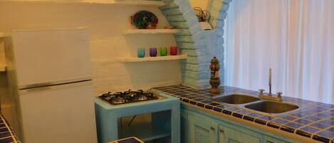 A kitchen with a blue tiled backsplash, a gas stove, a refrigerator, and a sink.