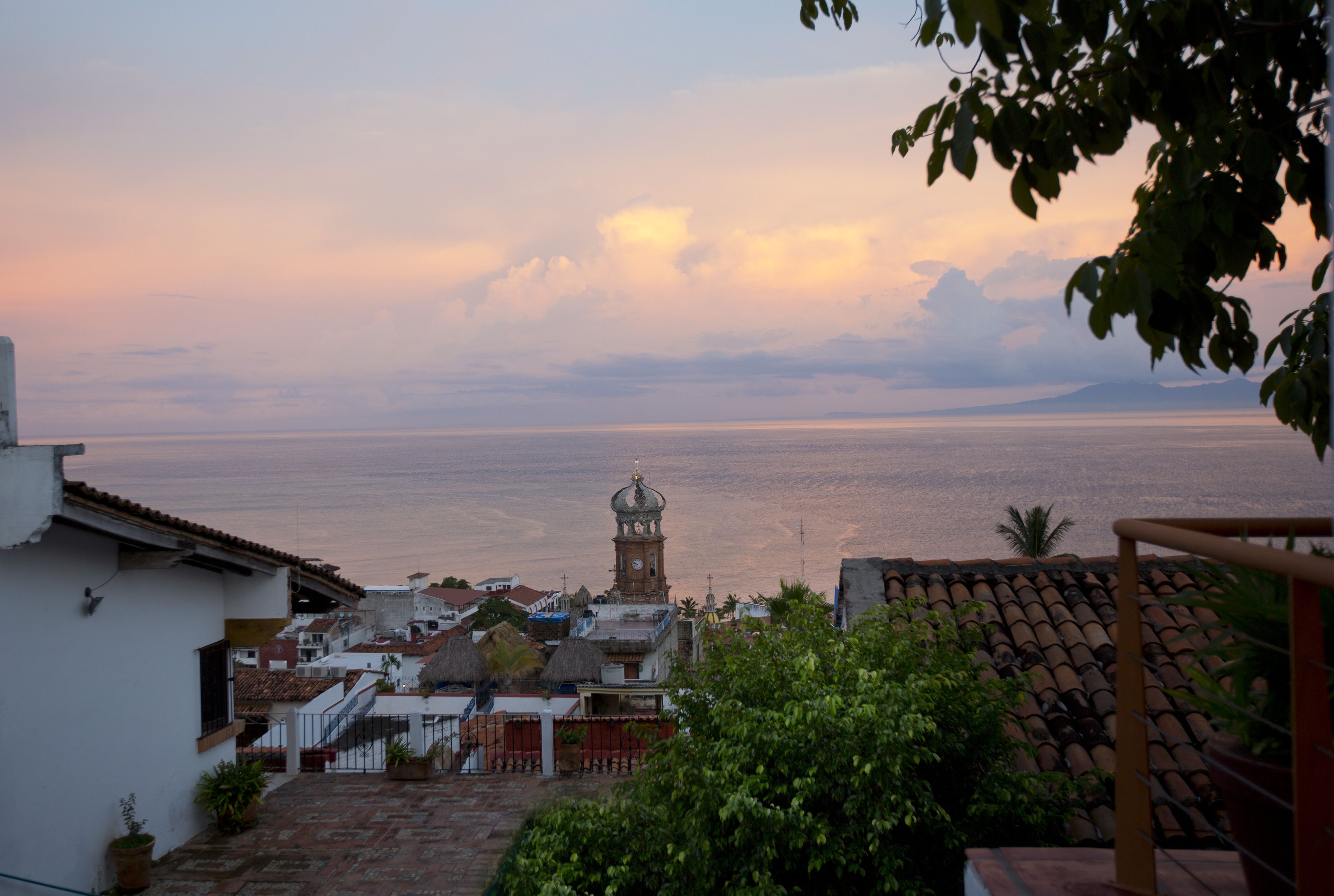 A coastal town with a prominent clock tower, terracotta rooftops, and a view of the sea.