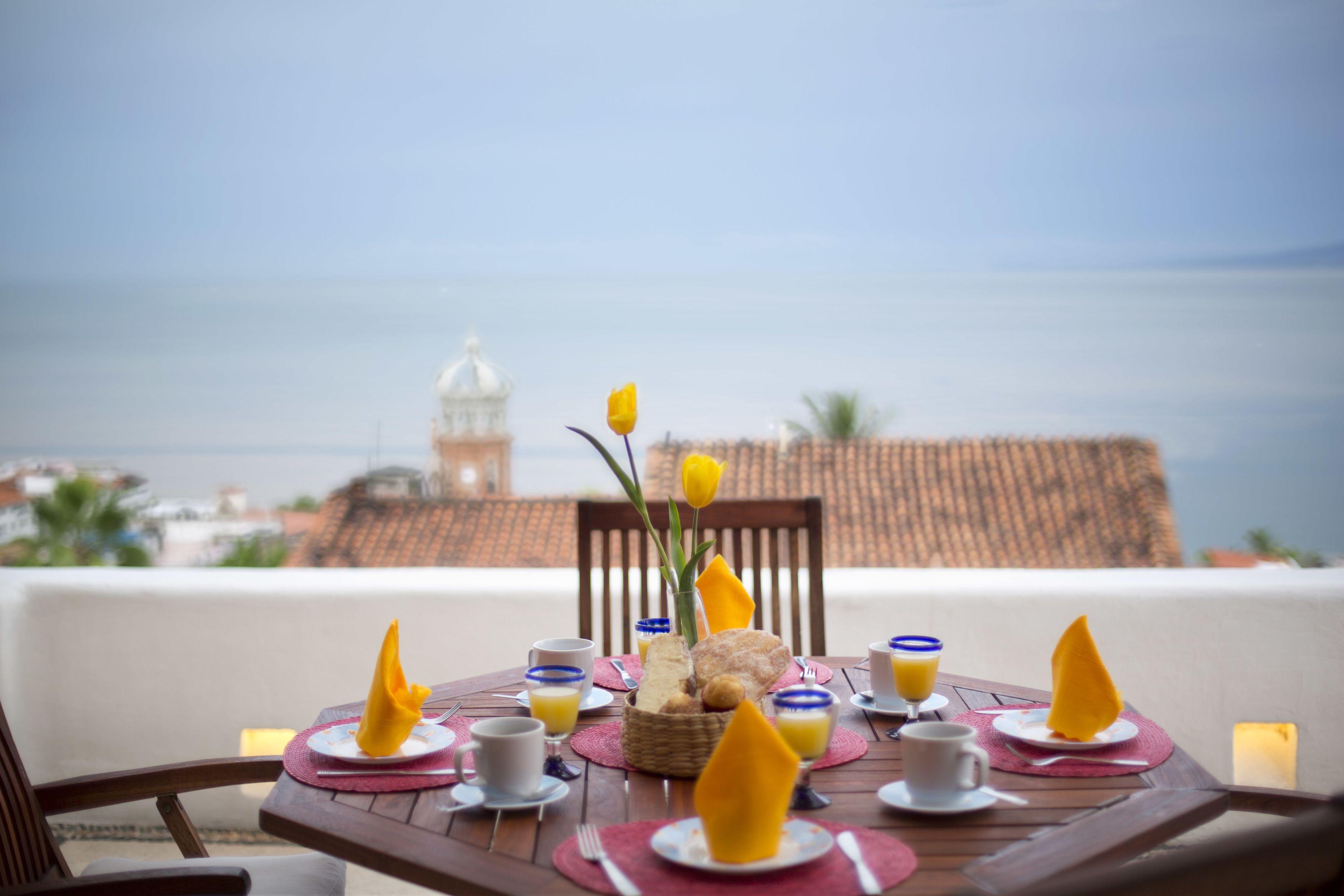 A table set for breakfast with a view of the sea and a building in the background.