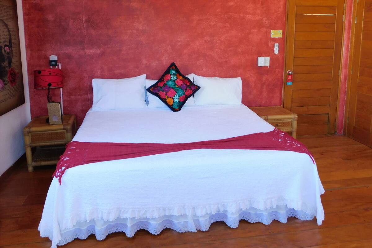 Ein Schlafzimmer mit einem großen Bett, einer roten Wand, einer Holztür und einem Nachttisch mit Lampe.