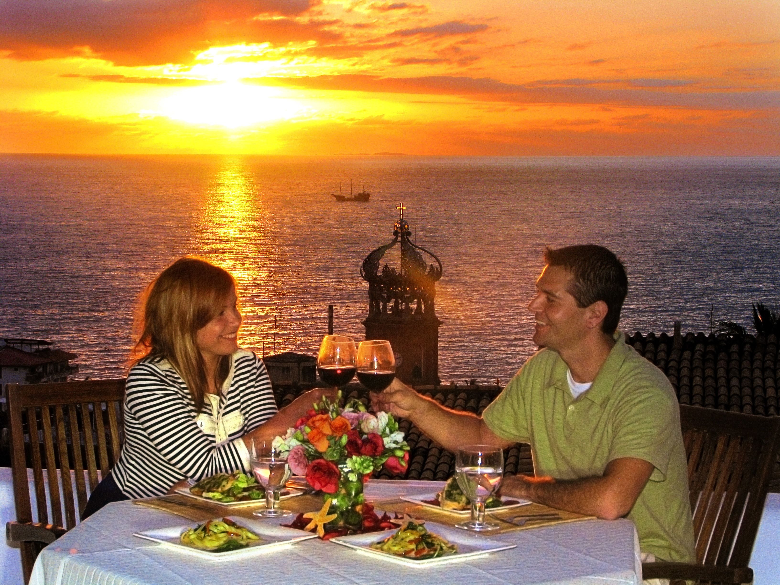 Un couple est assis à une table, profitant de la vue sur le coucher de soleil sur l’océan.