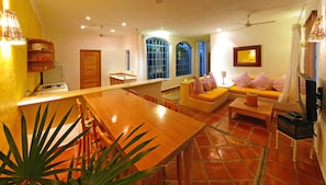 A spacious living area with a wooden dining table, a sofa set, and a television.