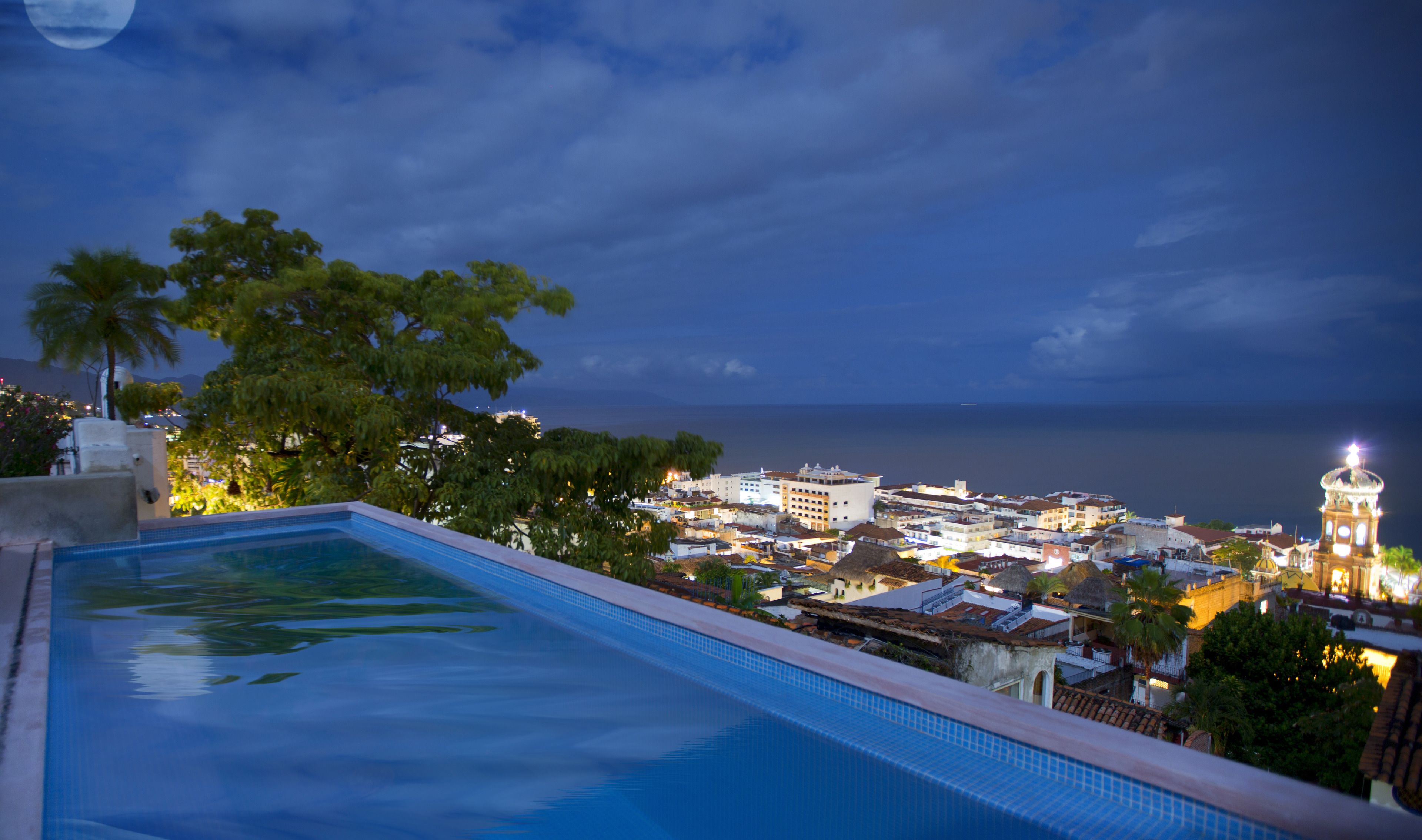 A swimming pool with a view of a coastal town at dusk.