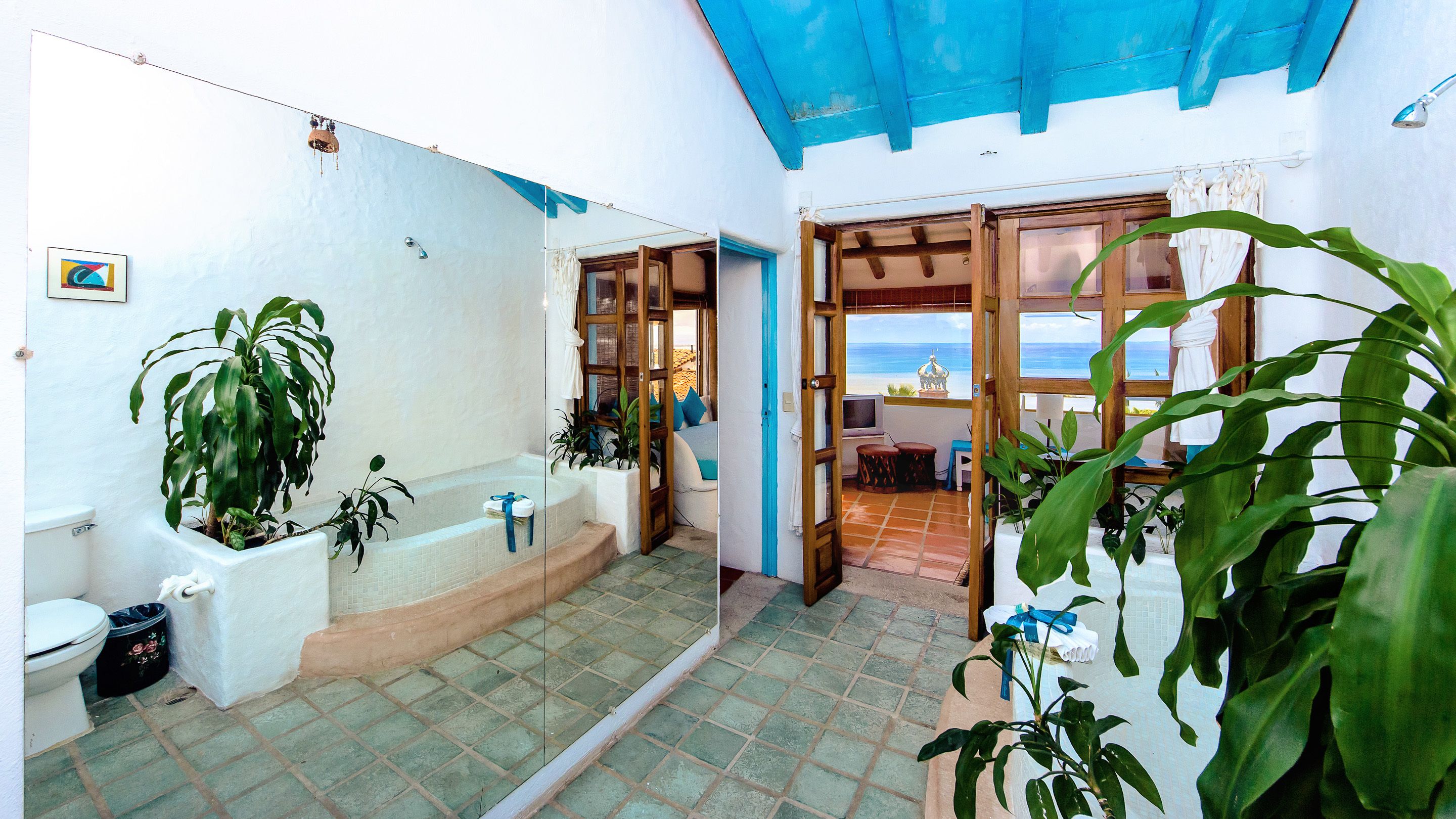 A bathroom with a bathtub, toilet, and sink, surrounded by potted plants.