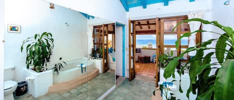 A bathroom with a bathtub, toilet, and sink, surrounded by potted plants.