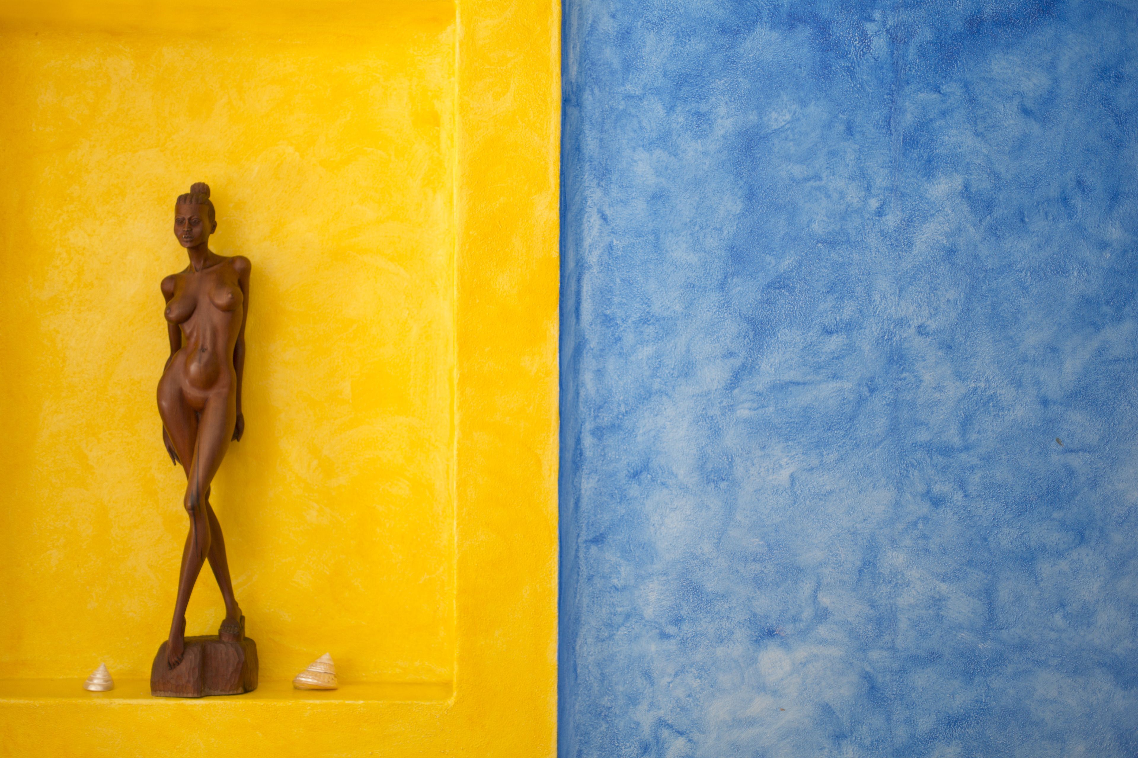 A statue on a pedestal against a yellow and blue wall.