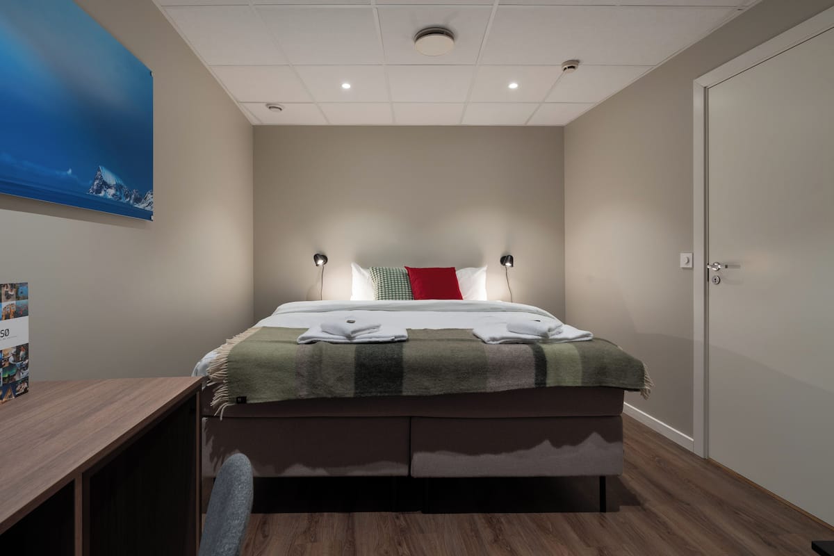 A modern bedroom with a bed, bedside lamps, a desk, and a door.