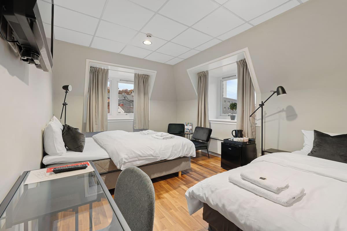A hotel room with two beds, a desk, a chair, a TV, and a window with curtains.