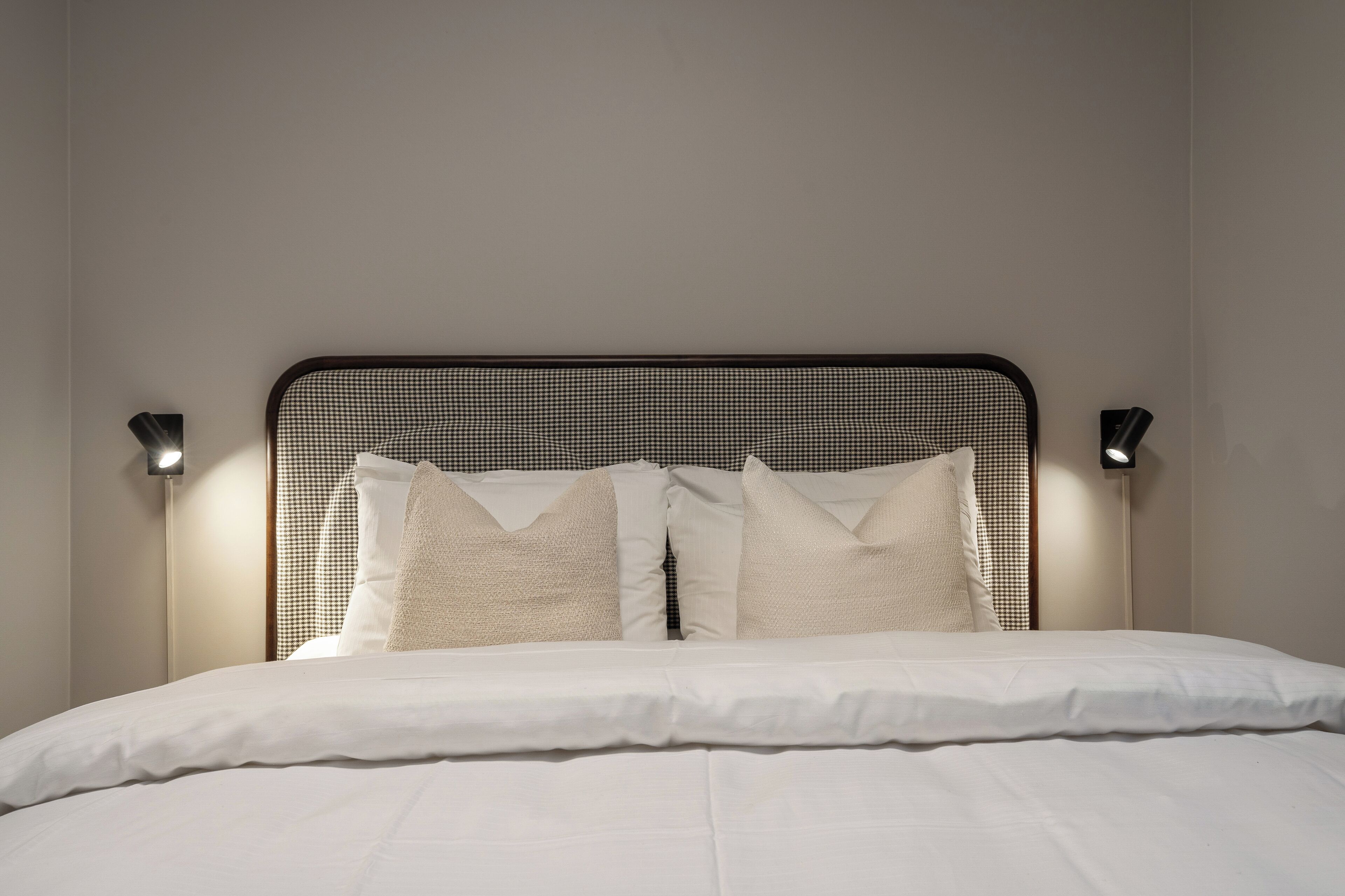 A neatly made bed with white linens and a black metal headboard.