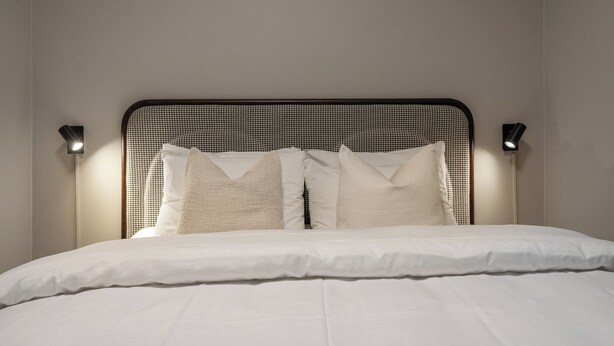 A neatly made bed with white linens and a black metal headboard. - First Hotel Skansen (Tromsø)