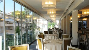 A restaurant with large windows, tables set for dining, and chandeliers.