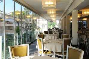 A restaurant with large windows, tables set for dining, and chandeliers.