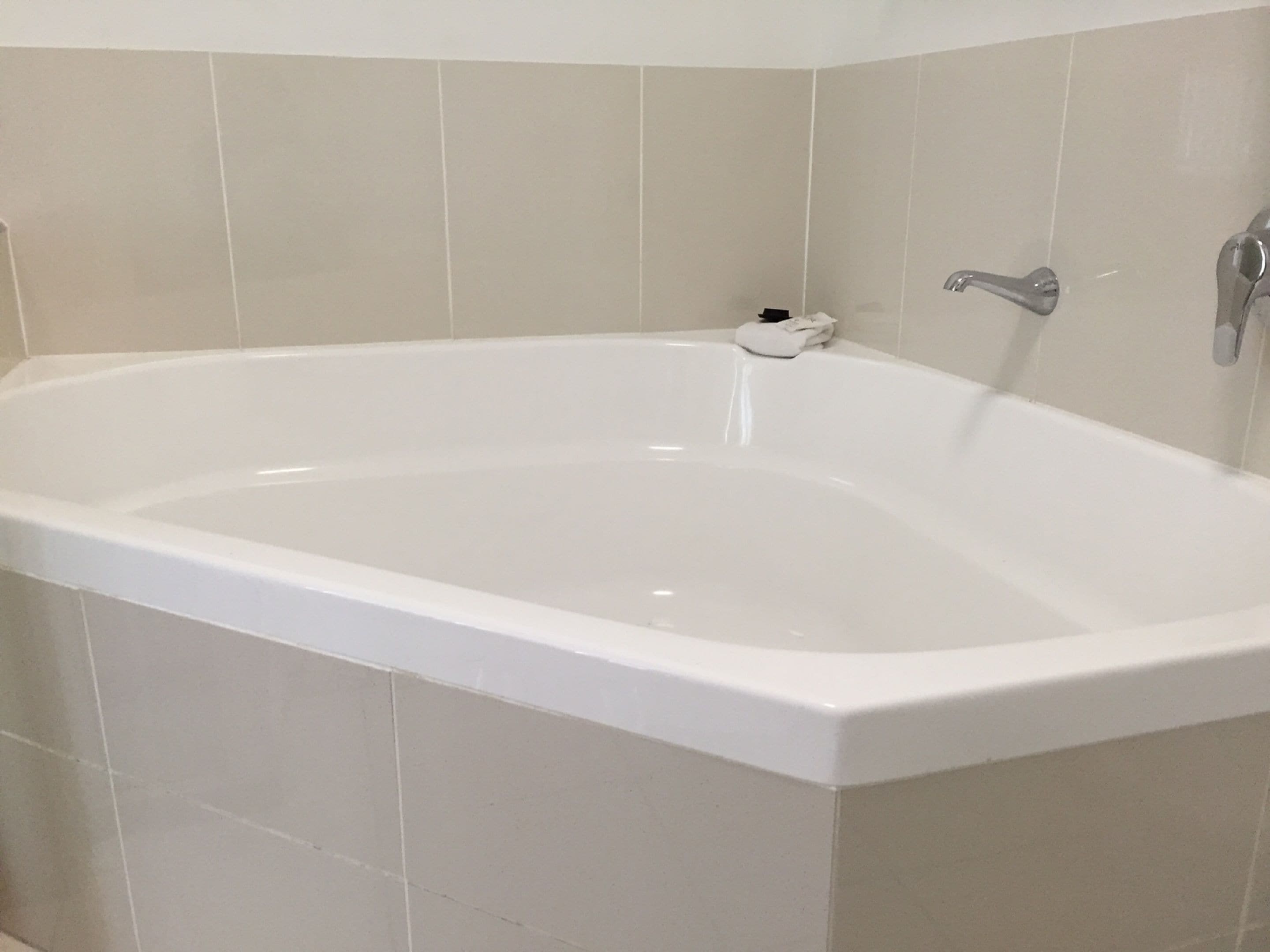 A white freestanding bathtub in a bathroom with beige tiled walls.