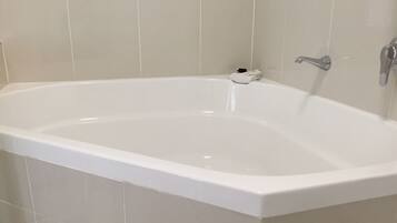 A white freestanding bathtub in a bathroom with beige tiled walls.