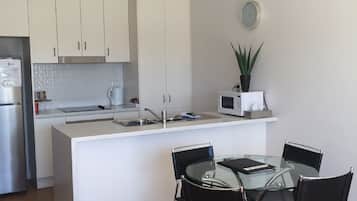A modern kitchen with white cabinets, a stainless steel refrigerator, a microwave, and a glass dining table with four chairs.