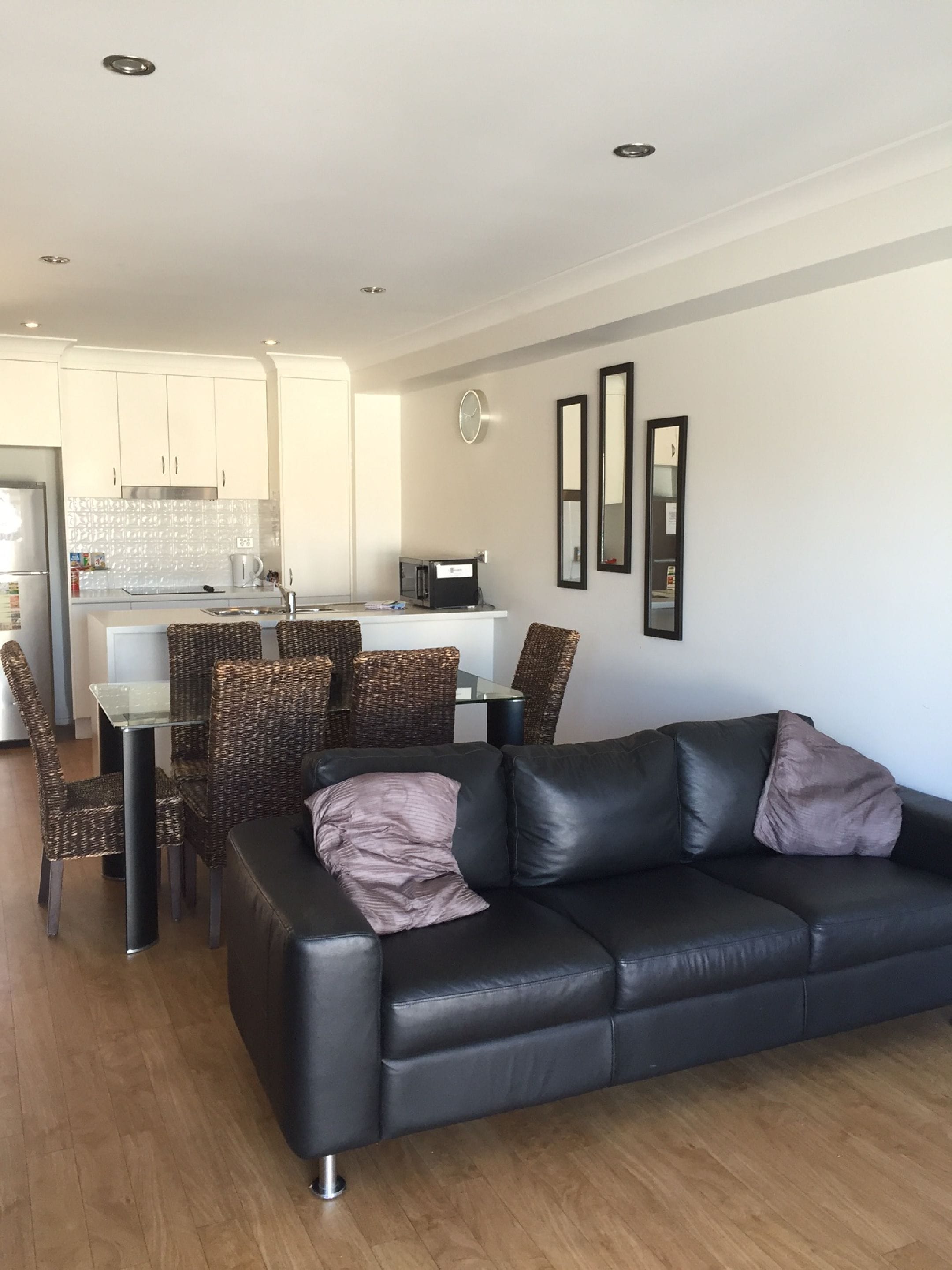A modern living room with a black leather sofa, wicker chairs, and a glass dining table.