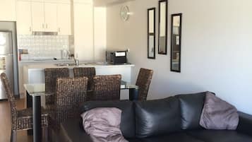 A modern living room with a black leather sofa, wicker chairs, and a glass dining table.