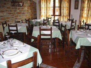 Un restaurante con varias mesas dispuestas para comer, con sillas de madera y manteles verde claro.