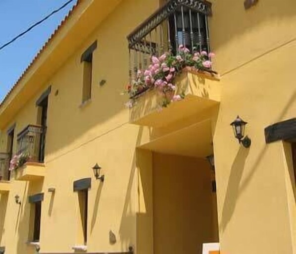 Un edificio amarillo con un balcón decorado con flores rosadas.